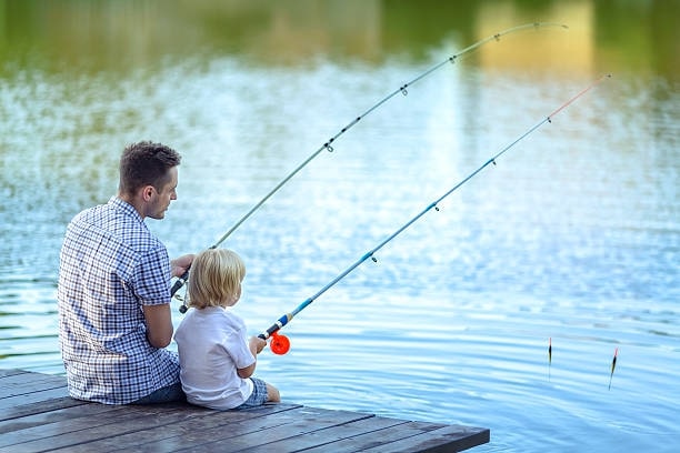 A dad and son fishing in the lake while sitting on the deck